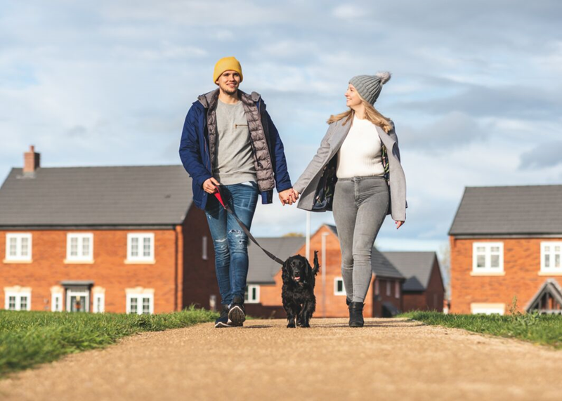 Couple walking dog in front of houses
