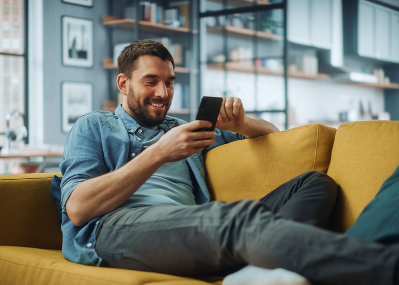 Man lying on sofa smiling at phone