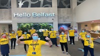 A Danske Bank branch team of 13 people stand socially distanced and with masks on. They have yellow AWARE t shirts on and all have their thumbs up! The 'Hello Belfast' light up sign is in the background.