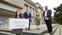 Image shows four people standing outside, at the front someone holds a sign about the digital academy.