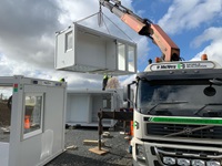P McVey Mobile Buildings Large lorry with a crane lifts a mobile unit into the air.